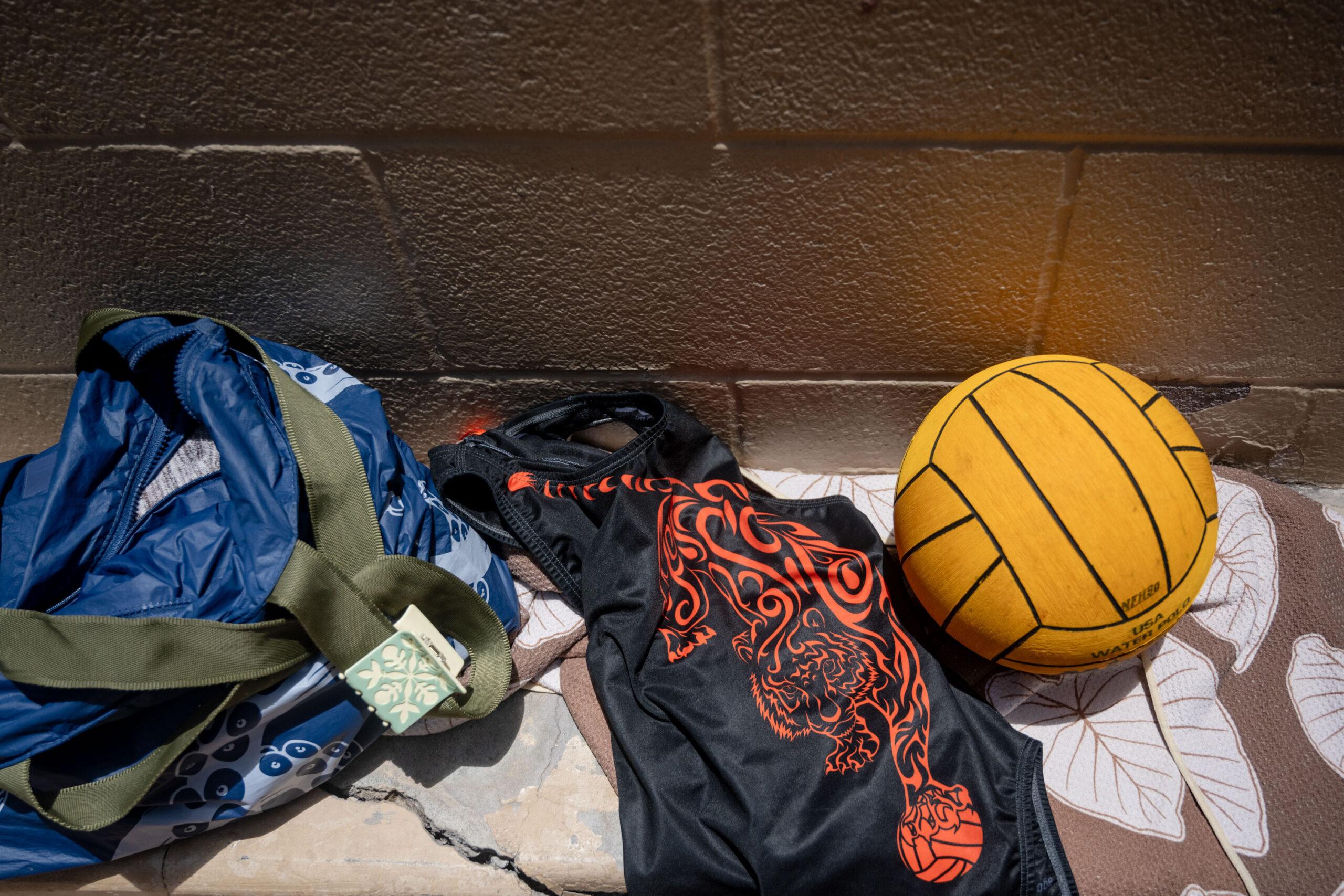 Photo of water polo ball, James Campbell High School one piece swimsuit, and changing bag on a bench outside of a a public women's bathroom at Ewa Beach in Honolulu, Hawaii.